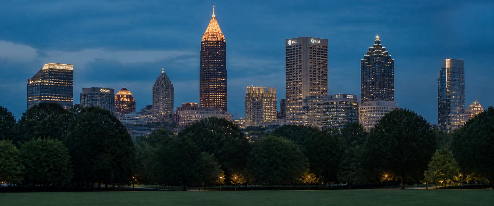 The Midtown Atlanta skyline at dusk seen from Piedmont Park, Bank of America Plaza's gold spire lit above the treeline